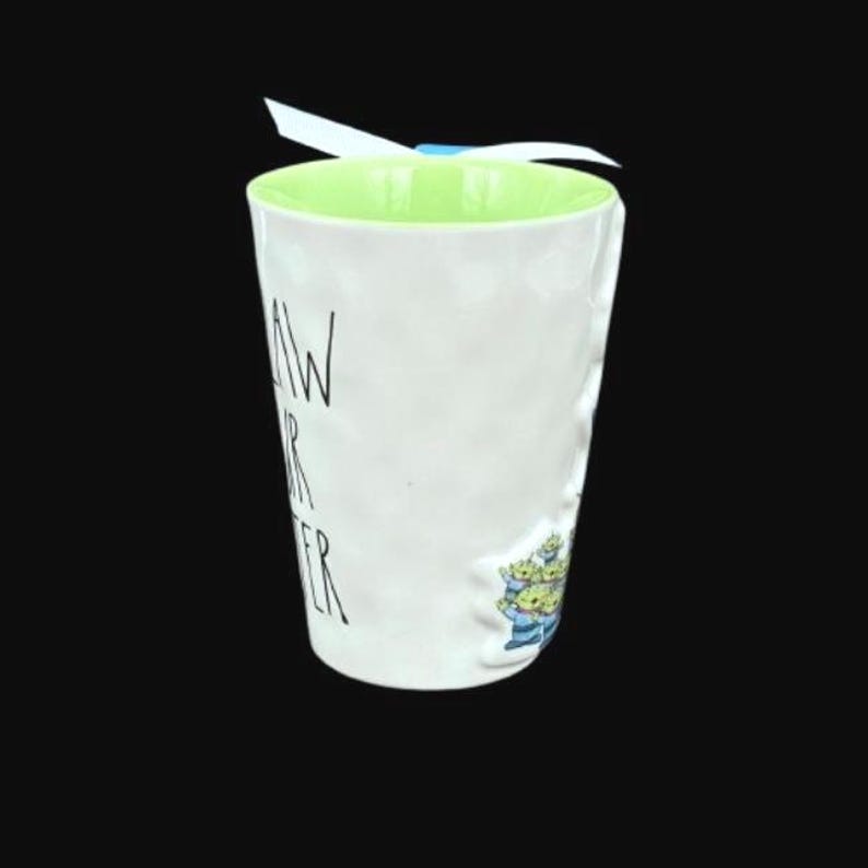 Puede incluir: Taza de cer&aacute;mica blanca con interior verde claro y exterior texturizado. La taza presenta el texto "AW YOUR SISTER" en letras negras y una peque&ntilde;a ilustraci&oacute;n de extraterrestres verdes. Una cinta blanca est&aacute; atada alrededor de la parte superior.