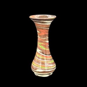 Puede incluir: Un jarrón decorativo con la parte superior ensanchada y una base bulbosa. El jarrón presenta un patrón arremolinado de rayas marrones, naranjas, blancas y verdes. El jarrón mide aproximadamente 20 cm de altura.