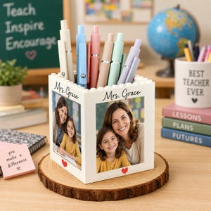 May include: A white square desk organizer constructed from interlocking plastic bricks, featuring two photo panels printed with the text Mrs. Grace and a small red heart. The organizer holds several colorful pens and sits on a round wood slice.
