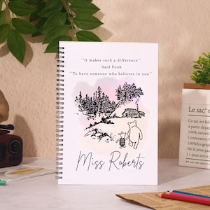 May include: A white spiral-bound notebook with a Winnie the Pooh illustration and the text "It makes such a difference" and "To have someone who believes in you." The notebook is personalized with the name "Miss Roberts."