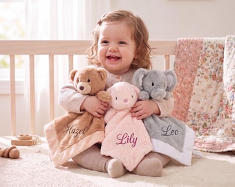 Puede incluir: Tres mantitas de seguridad de peluche con cabezas de animales: un oso marrón con el nombre Hazel, un animal rosa claro con el nombre Lily y un elefante gris con el nombre Leo. Cada manta cuadrada y suave tiene un nombre bordado.