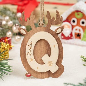 May include: Wooden Christmas ornament shaped like a reindeer, featuring the letter "Q" and the name "Quentin". The ornament is brown with a light wood accent and snowflake details. It is designed for festive decoration.