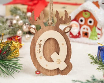 May include: Wooden Christmas ornament in the shape of a reindeer with the letter "Q" in the center. The name "Quentin" is engraved on the ornament. The ornament is brown with a light wood accent and snowflake details.