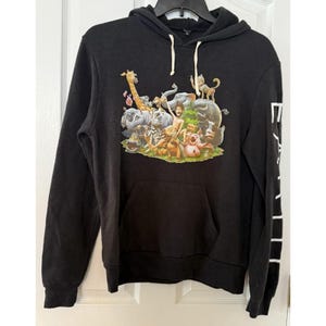 May include: Black hooded sweatshirt with a kangaroo pocket and white drawstring. The front features a colorful graphic of various animals and a person. White text is printed on the left sleeve.