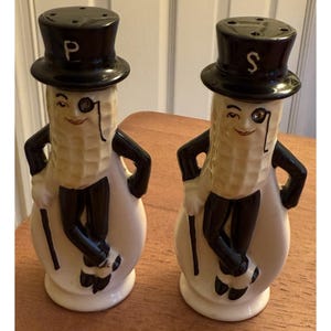 May include: A pair of vintage salt and pepper shakers shaped like Mr. Peanut. Each shaker is a cream color with black accents, a top hat, and a monocle. The "P" and "S" are on the top hats.