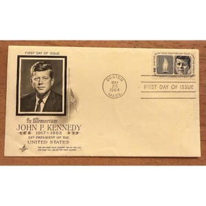 Pode incluir: Um envelope vintage comemorando John F. Kennedy, 35º Presidente dos Estados Unidos. O envelope apresenta um retrato de Kennedy, o texto "In Memoriam" e um selo "First Day of Issue" de Boston, 29 de maio de 1964.