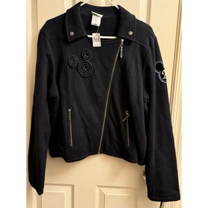 May include: Black zip-up jacket with a diagonal zipper and a small collar. The jacket has two zippered pockets and decorative embellishments, including a Mickey Mouse-themed design. A tag is attached to the jacket.