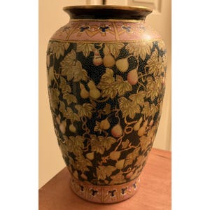 May include: A decorative ceramic vase with a dark blue background, adorned with gold-colored leaves and pear-shaped fruit. The vase has a pink band near the top and bottom with gold accents. The rim is dark brown.