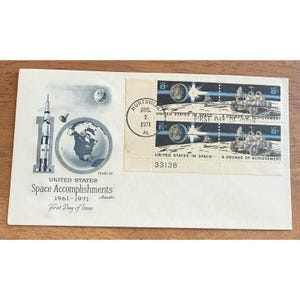 May include: A vintage envelope commemorating the United States Space Accomplishments from 1961-1971. The envelope features a stamp with a lunar rover, a rocket, and the Earth. The text reads "First Day of Issue" and "United States in Space".