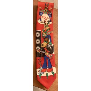 May include: Red novelty tie featuring a cartoon band of reindeer playing musical instruments. The reindeer are wearing sunglasses and playing a drum set, guitars, and a microphone. The words "ROCK ON" are printed on the drum set.