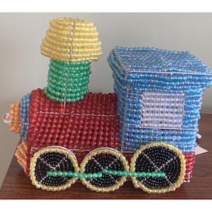 May include: A colorful beaded train toy. The train features a blue engine, a red body, and yellow, green, and orange accents. The wheels are black with yellow rims. The train is made of small, colorful beads.