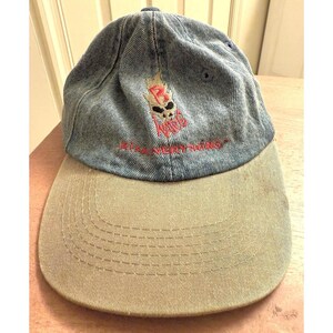 May include: A denim baseball cap with a khaki brim. The cap features a skull graphic with flames and the text "Rise Above Everything" in red. The hat is a classic style, suitable for casual wear.