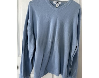 May include: A pale blue V-neck sweater hanging on a grey hanger. The sweater has long sleeves and a ribbed hem. The brand name "Old Navy" is visible on the tag. The sweater is made of a soft, knit material.