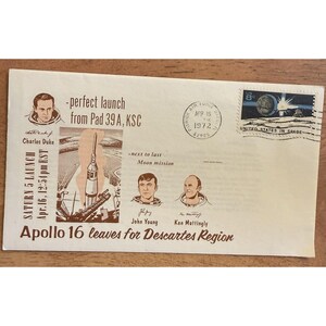 May include: An off-white envelope with a commemorative stamp and postmark from 1972. The envelope features illustrations of astronauts, a rocket launch, and the text "Apollo 16 leaves for Descartes Region."