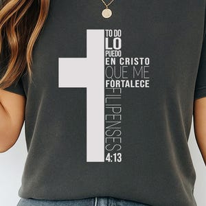 Puede incluir: Camiseta gris oscuro con un diseño de cruz blanca y el texto "TO DO LO PUEDO EN CRISTO QUE ME FORTALECE FILIPENSES 4:13". La camiseta tiene cuello redondo y mangas cortas.