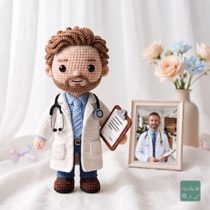 May include: A handcrafted crochet doll of a doctor with brown hair and a beard, wearing a white lab coat, blue shirt, blue tie, and blue trousers. The doll features a black stethoscope around the neck and holds a small brown clipboard.