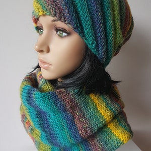 Peut inclure: Un ensemble bonnet et col tricoté dans un mélange de couleurs vives, dont le vert d'eau, le jaune, le violet et le bleu. Le chapeau est de style bonnet et le col est une écharpe circulaire. L'ensemble est présenté sur un mannequin.