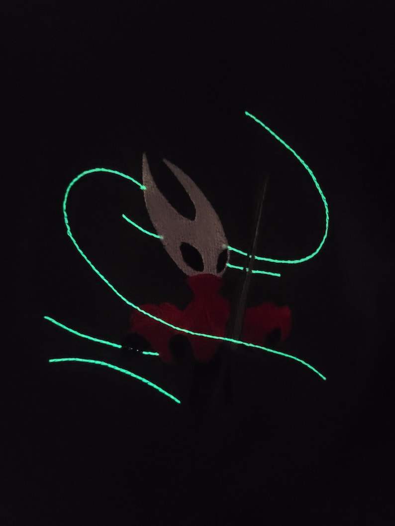 May include: A black background featuring a glowing green design of curved lines and a character with a white head, red body, and a black spear. The character has a mask with black eyes.