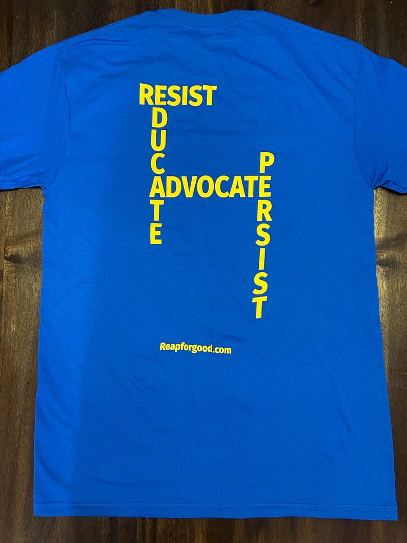 Op de afbeelding: Een koninklijk blauw T-shirt met de woorden "RESIST", "EDUCATE", "ADVOCATE" en "PERSIST" in het geel gedrukt, die een kruis vormen. De woorden "Reapforgood.com" zijn in het geel gedrukt aan de onderkant van het T-shirt.