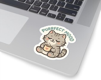 May include: A sticker featuring a cartoon cat holding a cup of coffee. The cat is gray with black stripes and closed eyes, and the cup is beige. The sticker has the words "PURRFECT MOOD" in a light green color.