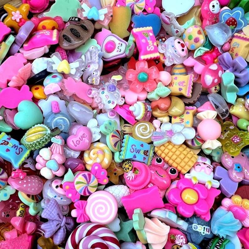 May include: A vibrant assortment of colorful resin charms in various shapes, including candies, flowers, hearts, and bows. The charms are in shades of pink, purple, yellow, and blue, with some featuring the word "Sweet". These decorative embellishments are ideal for crafting and jewelry making.