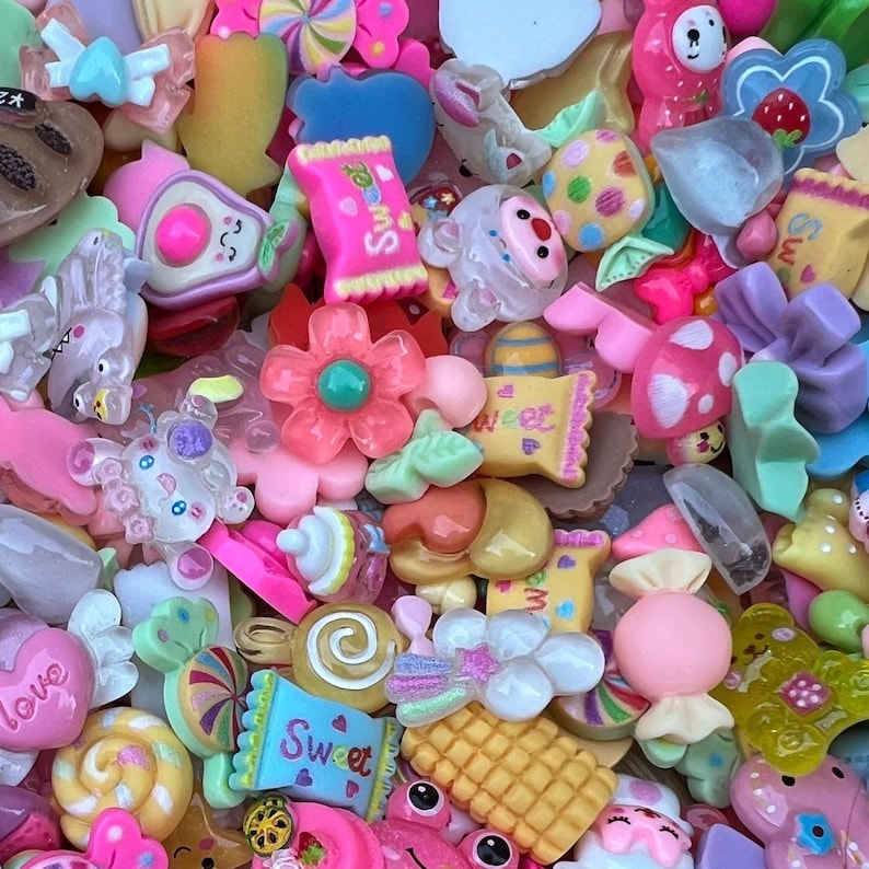 May include: A vibrant assortment of colorful resin charms in various shapes. The collection includes candies, flowers, hearts, and other whimsical designs in shades of pink, yellow, blue, and green. Some charms have the word "Sweet" on them.