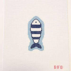 May include: A needlepoint canvas featuring a centered fish motif stitched in alternating dark blue and white horizontal stripes, surrounded by a light blue outline. The letters EFD are stitched in red in the bottom right corner of the white grid.