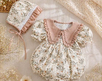 May include: A cream-colored romper and matching bonnet set featuring a botanical print of green leaves and small orange berries. The romper has short puff sleeves, a large dusty rose ruffled collar, and the bonnet includes lace trim.