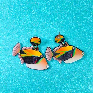 Handmade rectangular triggerfish earrings crafted from shrink plastic with a glossy UV resin front. These lightweight dangle earrings feature bold rectangular triggerfish with striking black bodies, bright yellow markings, and electric blue accents inspired by tropical reef life. Eye-catching and unique, they add a vibrant ocean vibe—perfect for marine life lovers and statement jewelry fans. By Moon Shark Creations.