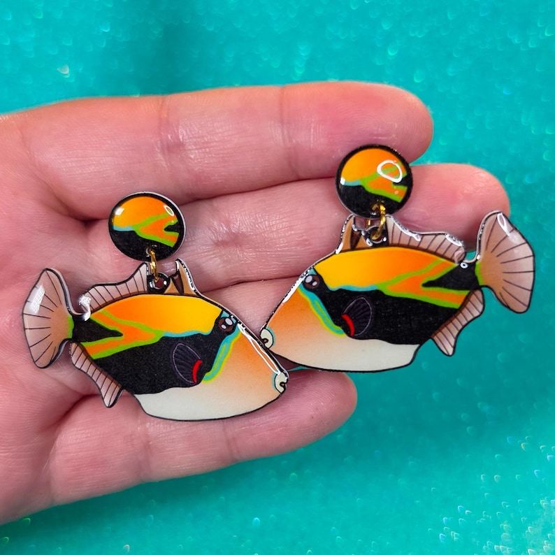 Handmade rectangular triggerfish earrings crafted from shrink plastic with a glossy UV resin front. These lightweight dangle earrings feature bold rectangular triggerfish with striking black bodies, bright yellow markings, and electric blue accents inspired by tropical reef life. Eye-catching and unique, they add a vibrant ocean vibe—perfect for marine life lovers and statement jewelry fans. By Moon Shark Creations.