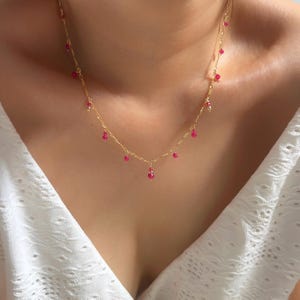 Peut inclure: Un délicat collier en or orné de petites pierres précieuses roses vibrantes. Le collier a une fine chaîne et les pierres précieuses sont espacées uniformément, créant un design subtil mais accrocheur. C'est un bijou.