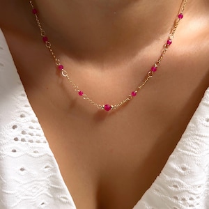 May include: A gold chain necklace with small pink beads. The necklace is delicate and feminine.