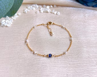 May include: Delicate gold bracelet featuring small white pearls and a vibrant blue gemstone. The bracelet is connected by a delicate gold chain and has a small pearl charm near the clasp. A beautiful piece of jewelry.