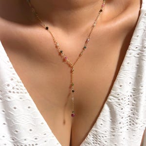 Puede incluir: Un collar de cadena en tono dorado con un diseño en forma de Y. La delicada cadena está adornada con pequeñas cuentas de piedras preciosas multicolores en tonos rosa, verde, azul y transparente, espaciadas a lo largo de los eslabones y el colgante.