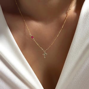 May include: A gold chain necklace with a small cross pendant and a single red gemstone accent.