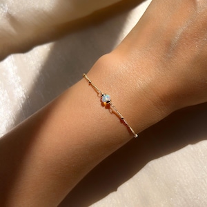 May include: A delicate gold chain bracelet with a single opal gemstone. The opal is a milky white color with iridescent flashes of color.