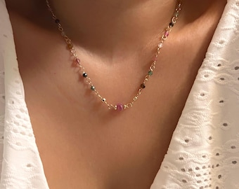 Pode incluir: Um colar de corrente de ouro com pequenas pedras preciosas coloridas. O colar é delicado e apresenta uma variedade de cores, incluindo rosa, verde e preto.