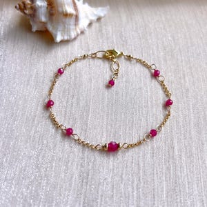 May include: A delicate gold chain bracelet with small pink gemstones. The bracelet has a lobster clasp closure.