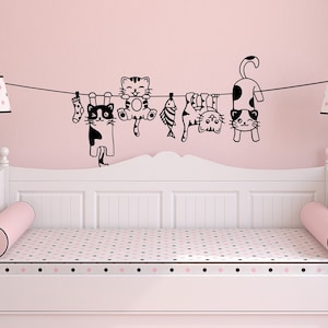 May include: A white daybed with a pink and black polka dot patterned mattress and two pink cylindrical pillows. A black and white cat-themed wall decal with five cats hanging on a clothesline is above the daybed.