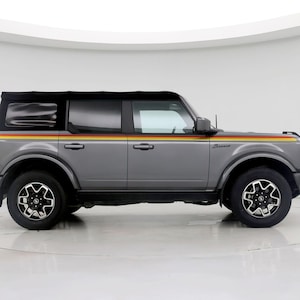 May include: A grey SUV with a black roof and black wheels. The vehicle features a colourful stripe design in red, yellow, and orange along the side. The word "Bronco" is visible on the side.