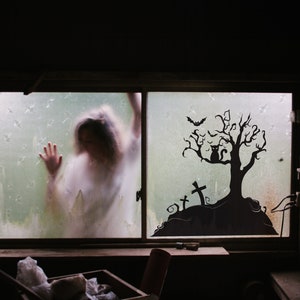 May include: A silhouette of a spooky tree with a black cat sitting on a branch, bats flying overhead, and a graveyard with crosses in the background. The tree is on a foggy window pane with a blurry figure in the background.