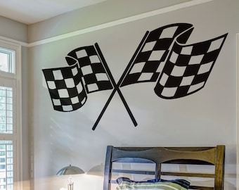 May include: Black and white checkered racing flags crossed over each other on a white wall. A bed with a blue and white striped pillow is in the foreground.