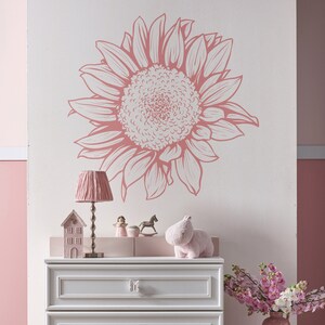 Puede incluir: Una c&oacute;moda blanca con tres cajones y pomos con forma de mariposa. La c&oacute;moda est&aacute; decorada con una calcoman&iacute;a de pared de girasol rosa y blanco. Una figura de hipop&oacute;tamo rosa se sienta encima de la c&oacute;moda.