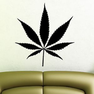 May include: A black silhouette of a marijuana leaf on a white wall above a green couch.