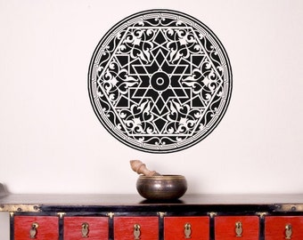 May include: A black and white circular wall decal with an intricate geometric design. The decal is mounted on a white wall above a red cabinet with multiple drawers. A small bronze bowl and wooden pestle sit on the cabinet.