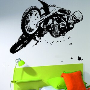 May include: Black and white silhouette of a motocross rider performing a stunt on a dirt bike. The rider is in mid-air, with the bike's front wheel off the ground. The image is set against a white background.