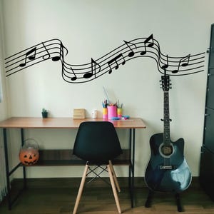 May include: Acoustic guitar in a room with a desk, chair, and musical notes wall art. The black guitar is on a stand. A black chair sits in front of a wooden desk. Black musical notes are on the wall.