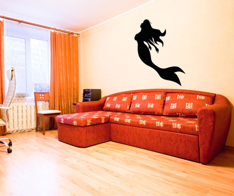 May include: A red sectional sofa with white patterned cushions in a living room with a black silhouette of a mermaid on the wall.