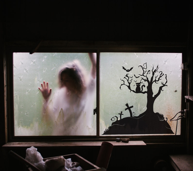 May include: A silhouette of a spooky tree with a black cat sitting on a branch, bats flying overhead, and a graveyard with crosses in the background. The tree is on a foggy window pane with a blurry figure in the background.