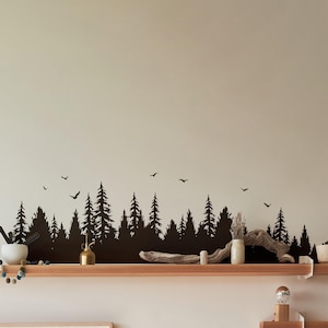 May include: Black silhouette wall decal of a forest with trees and birds. The decal is placed on a wall above a wooden shelf with decorative items.